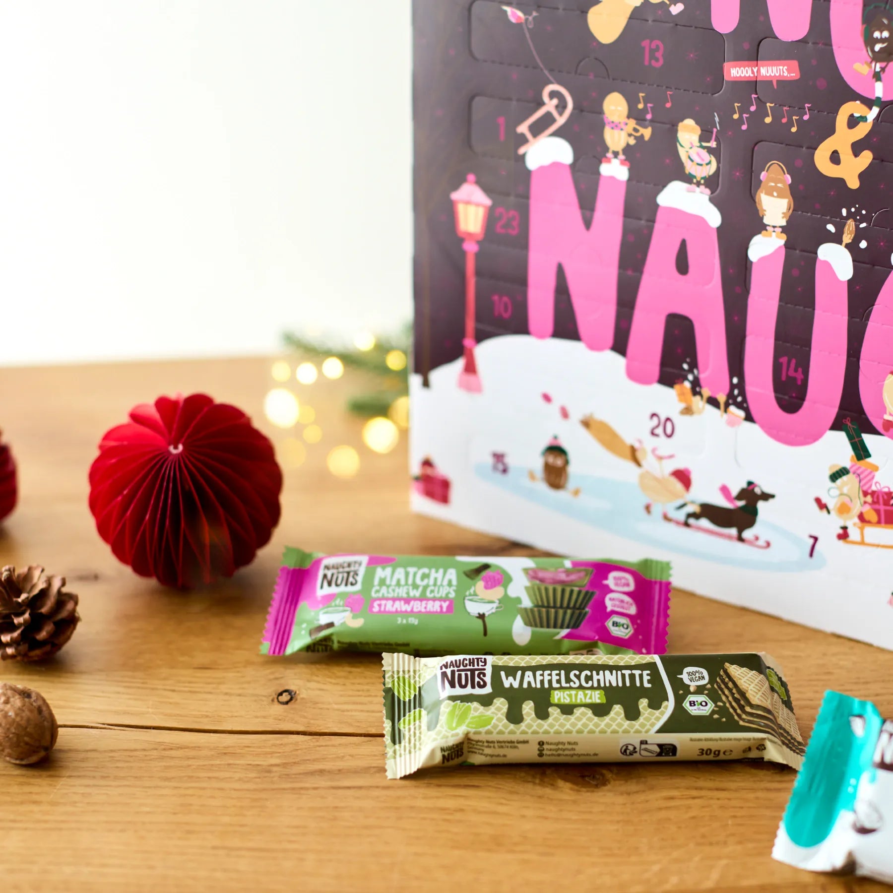 Adventskalender Classic 2026 mit Naughty Nuts Riegeln und weihnachtlicher Dekoration auf einem Holztisch