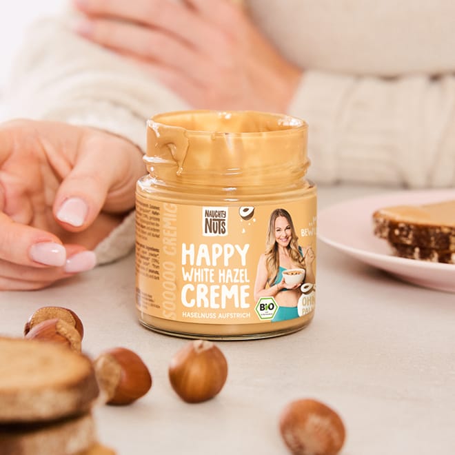 Happy White Hazel Creme Glas mit Haselnüssen und Toast im Hintergrund